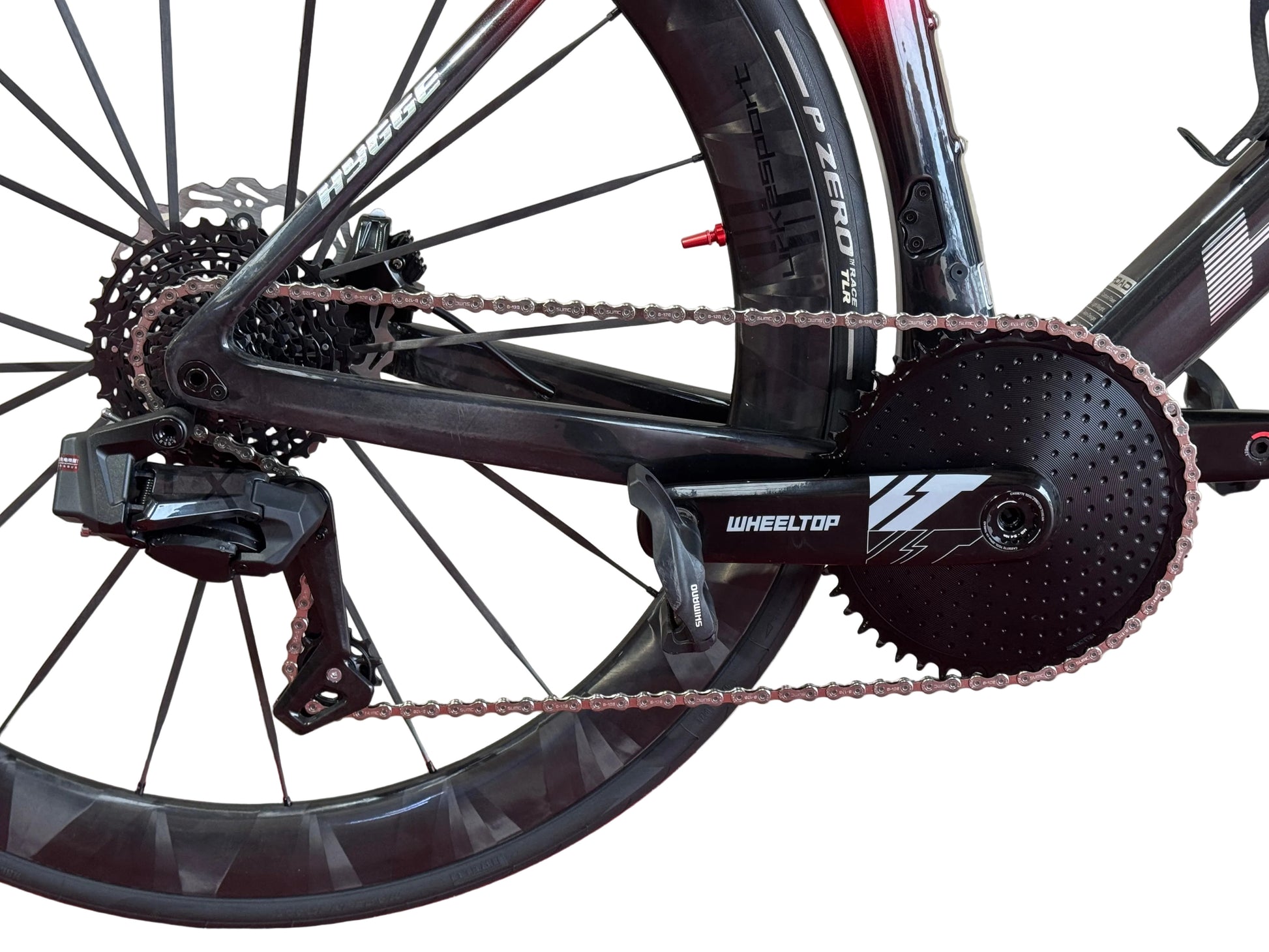 Close-up of a bicycle's rear wheel and drivetrain, showing a black Wheeltop chainring, cassette, derailleur, and black carbon fiber wheel with red accents.